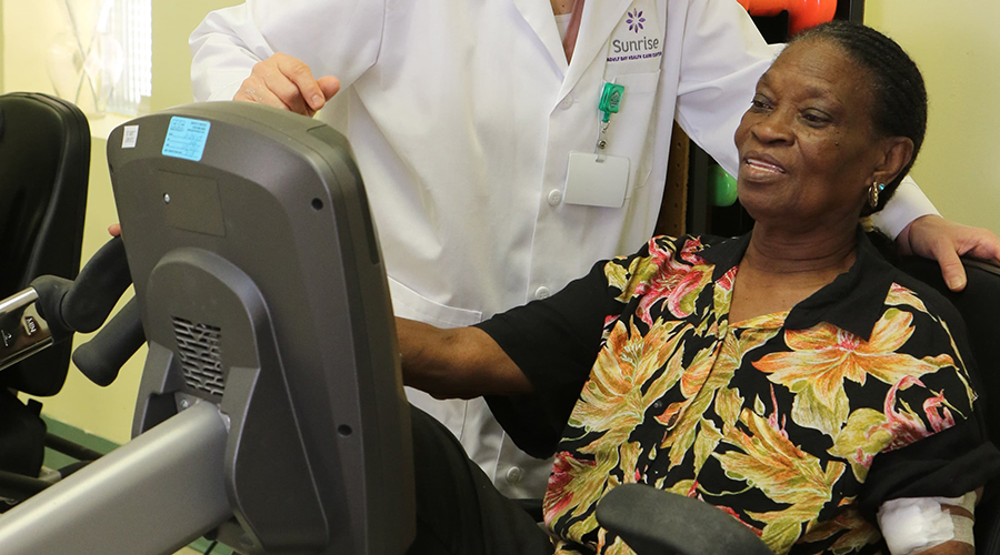 Woman on an exercise bike working with a physical therapist at Four Seasons Adult Day Care Center in Sunrise.