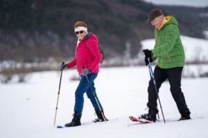 An older woman and man snowshoe through a wintery scene.