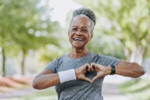 Older woman holds her hands in the shape of a heart in front of her chest.