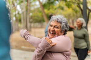 An older woman smiles and stretches outdoors as she prepares to have fun with friends.