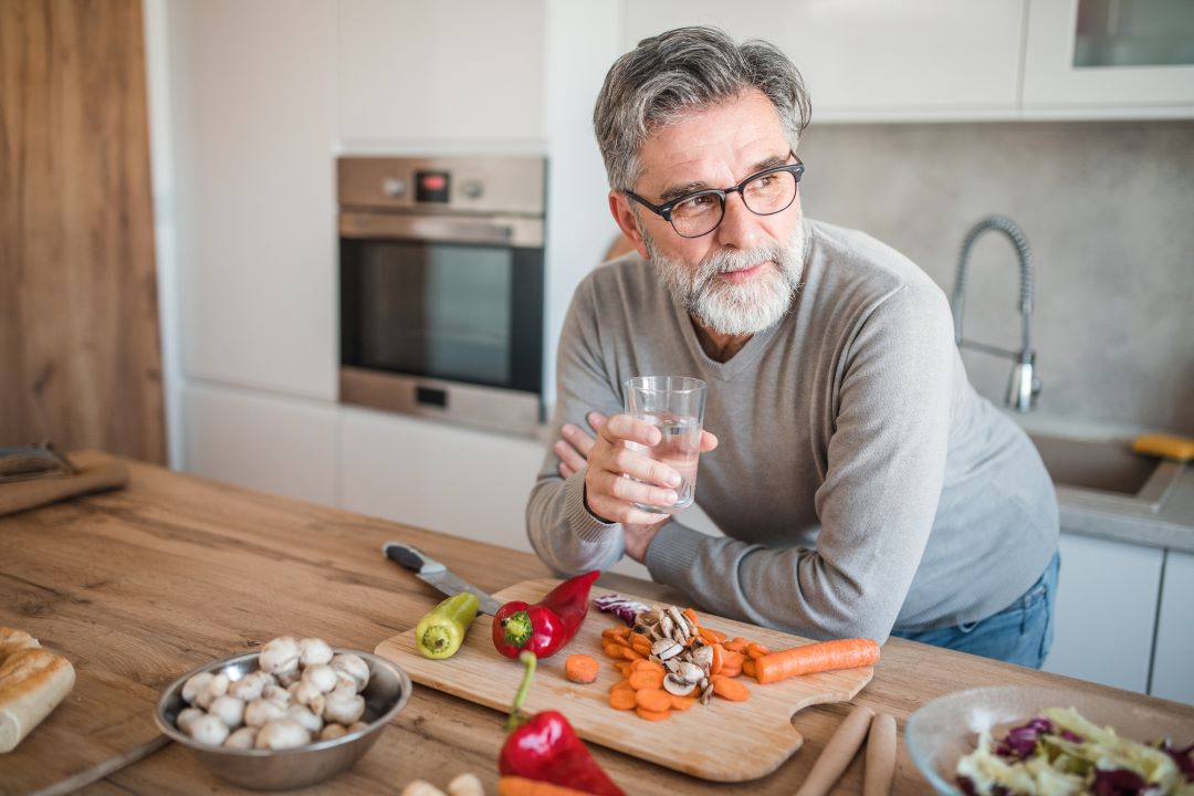 Older man drinks a glass of water as he prepares a kidney-friendly meal.