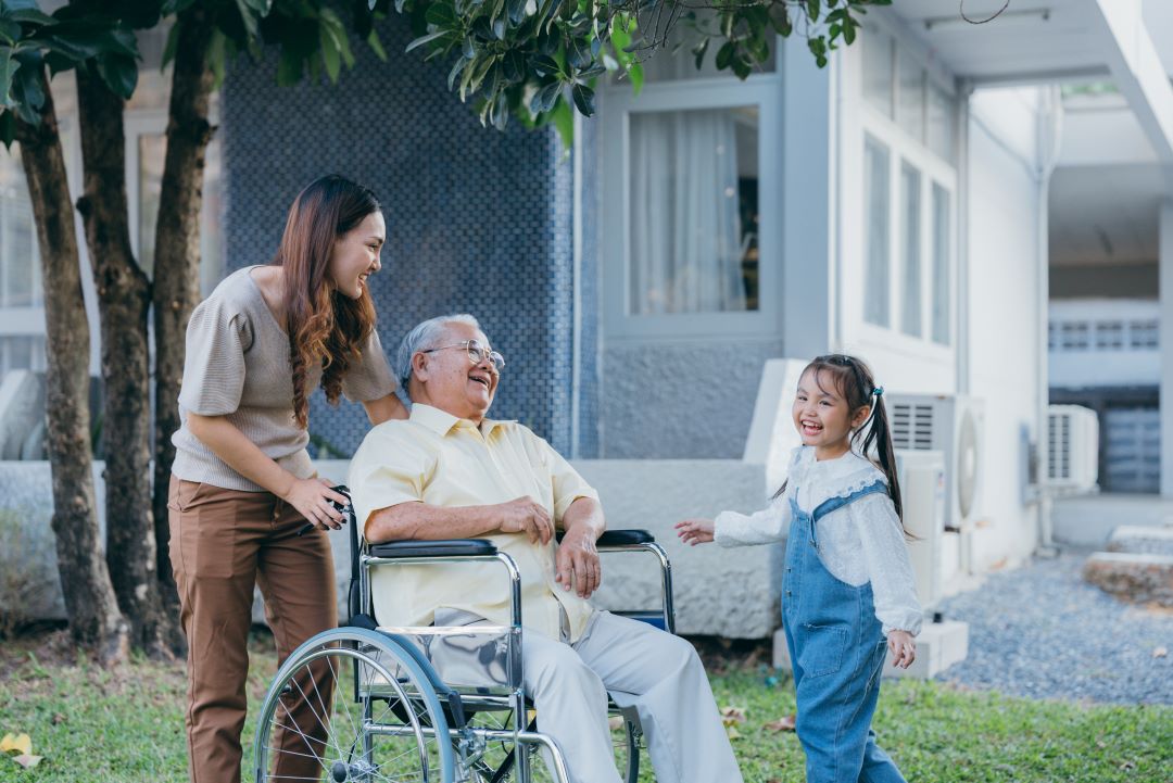 A female caregiver laughs with her father and child.