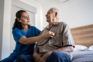 A caregiver listens to an older man's heart as he recovers at home.