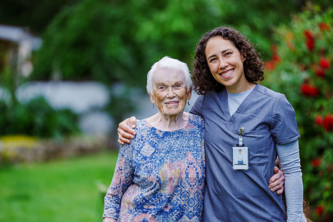 An older woman smiles alongside her caregiver.