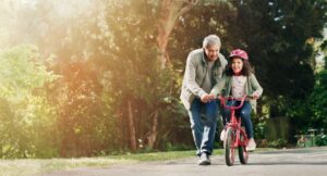 A grandfather teaches his granddaughter to ride a bike.